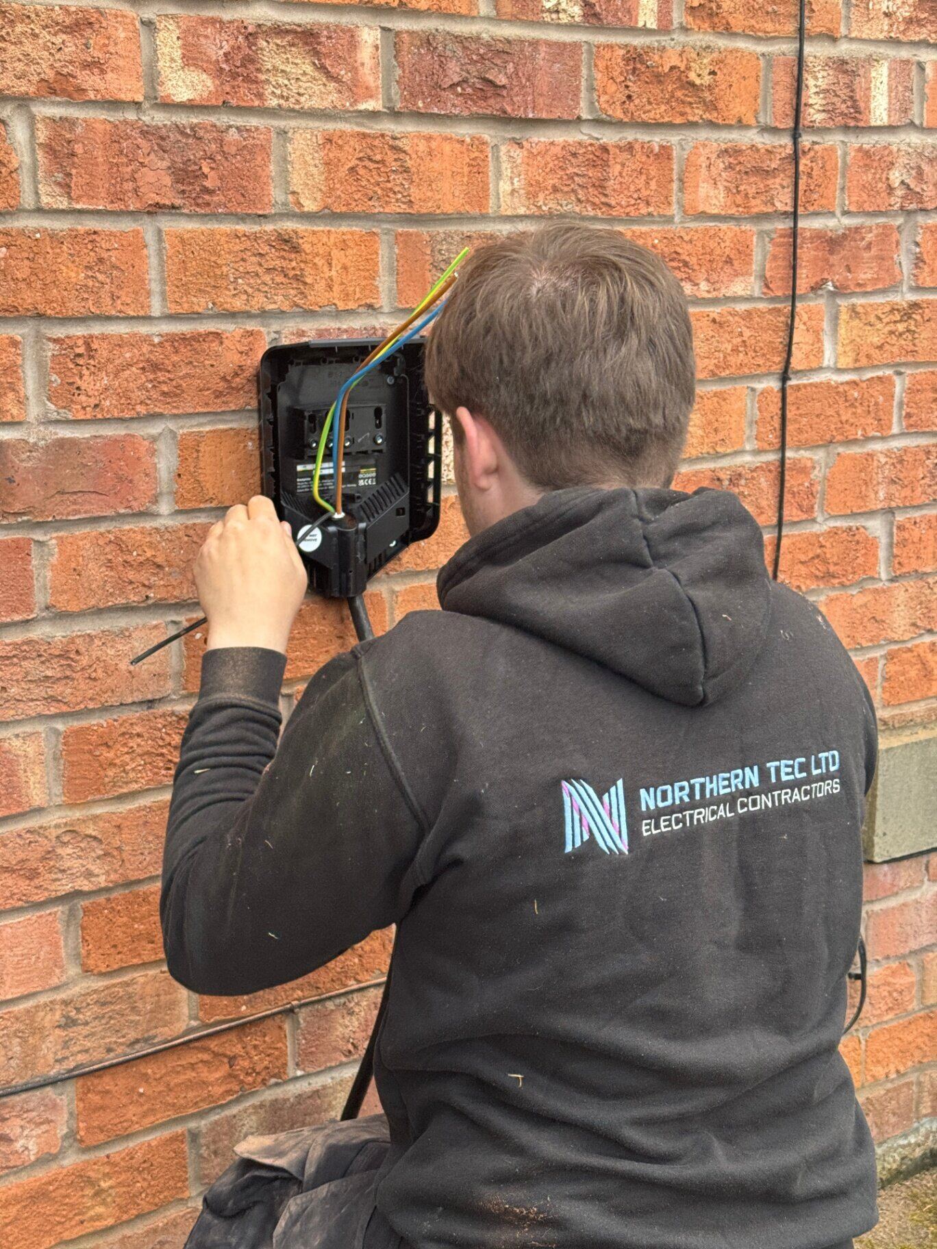 Northern Tec electrician wiring in a new home EV charge point on a brickwork facade