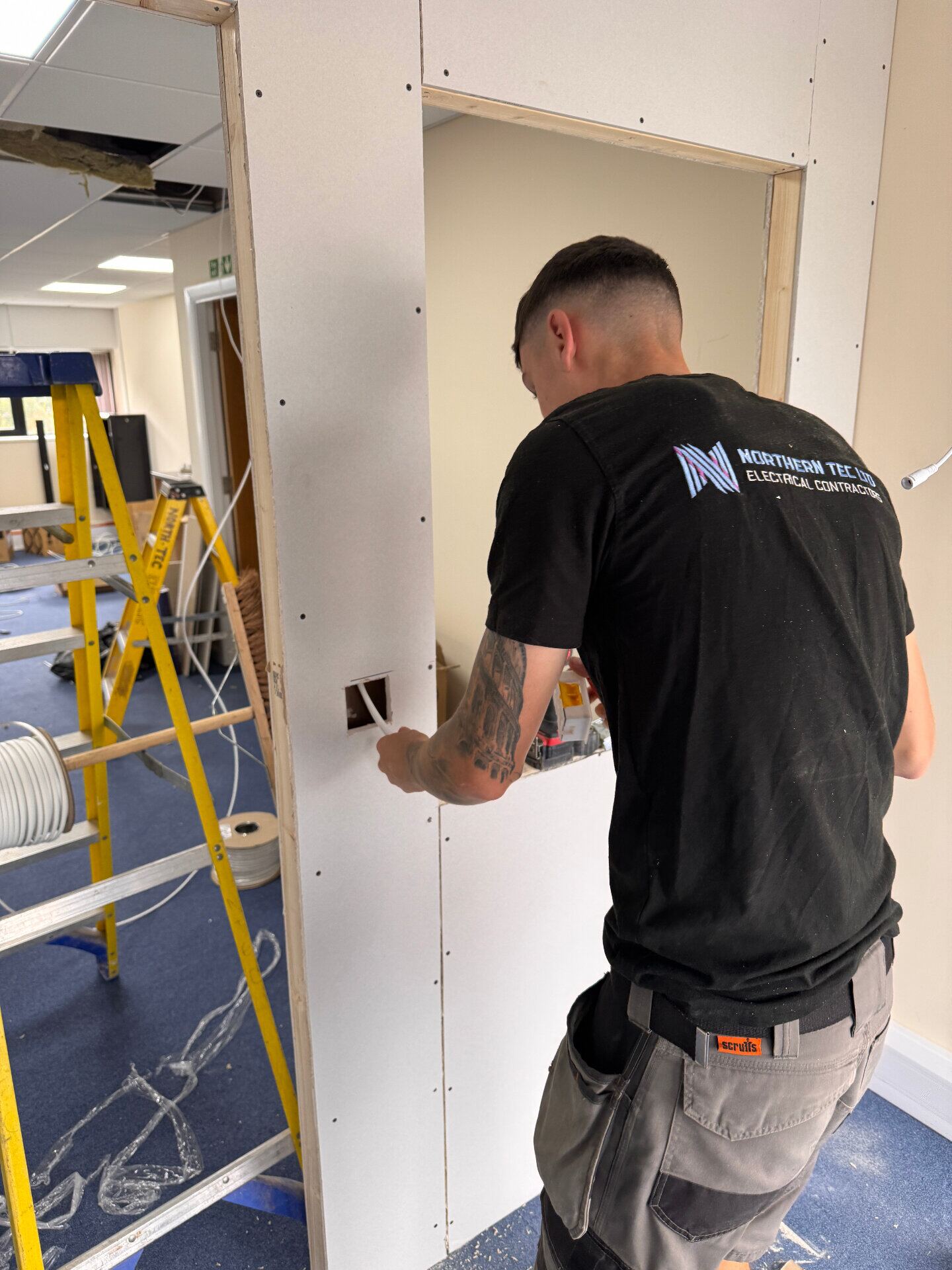 Northern Tec electrician first-fixing socket cabling through a new stud partition wall on a commercial fit-out