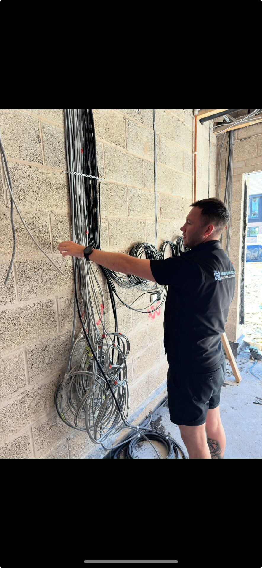Northern Tec electrician dressing first-fix cabling on a blockwork wall during a new-build project